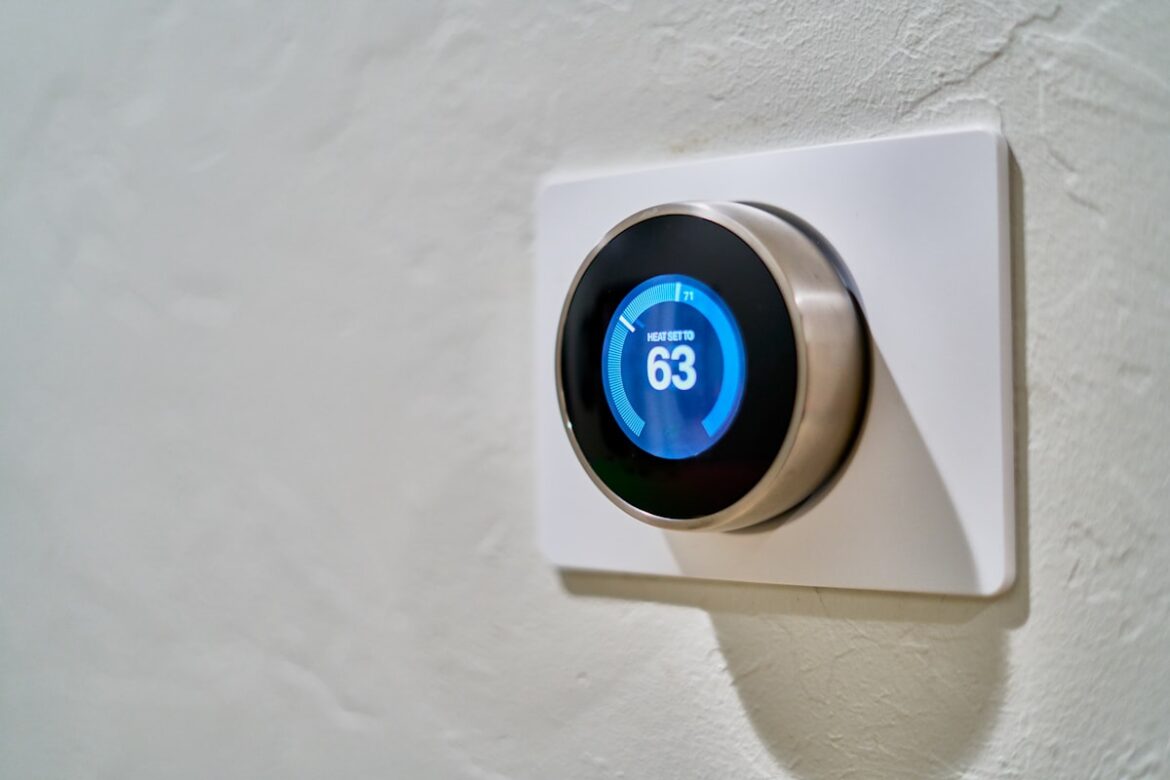 Smart thermostat on wall showing temperature control and energy savings app